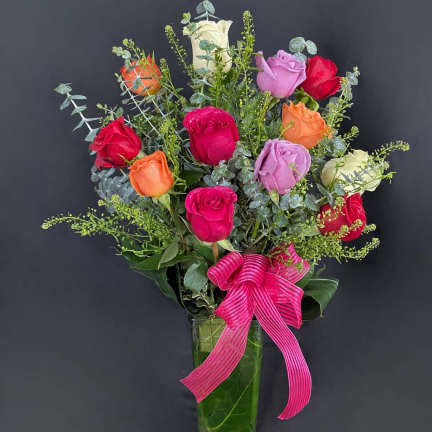 Mixed roses in a tall glass vase with a pink ribbon bow
