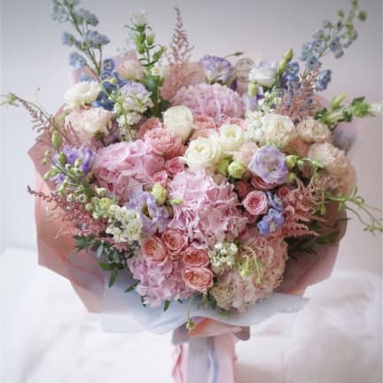 Large pastel bouquet of pink, white, and lavender flowers wrapped in pink paper