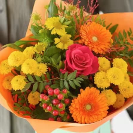 Bouquet of orange and yellow flowers with a pink rose in orange wrap