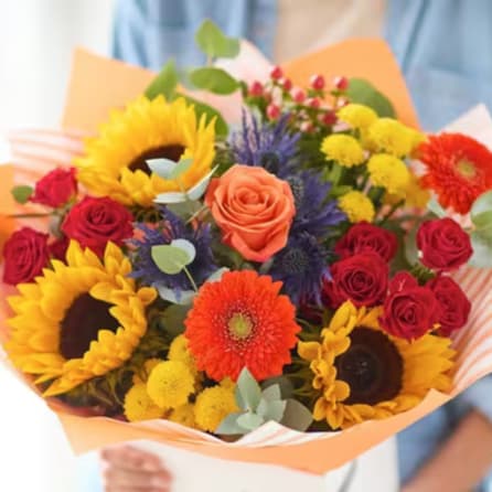 Mixed bouquet with sunflowers, roses, and gerbera daisies in orange wrap