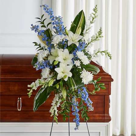 White lilies and blue flowers arranged on a casket spray