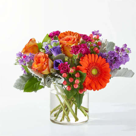 Mixed bouquet of orange, purple, and pink flowers in a clear glass vase