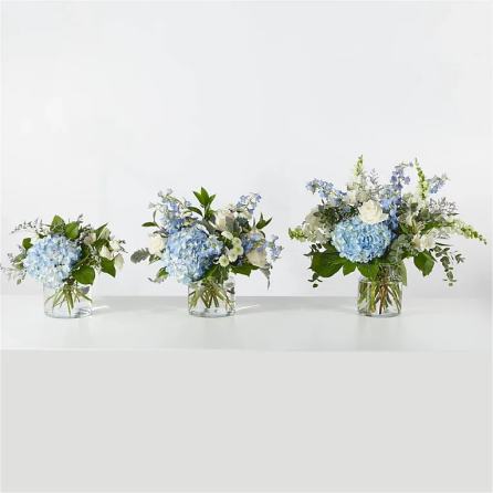 Three blue and white floral arrangements in clear glass vases