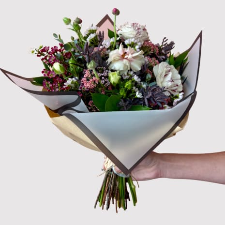 Handheld bouquet of white and pink flowers wrapped in paper