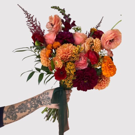 Hand-tied bouquet of peach, red, and orange flowers with a dark ribbon
