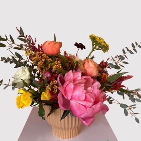 Mixed bouquet in a ribbed beige vase with pink, peach, yellow, and white blooms