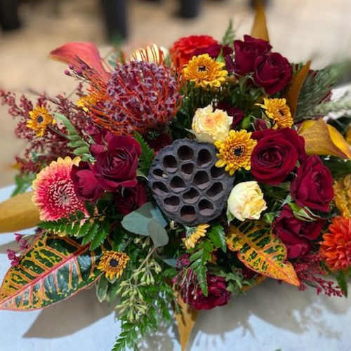 Mixed bouquet with red roses, yellow daisies, and tropical foliage