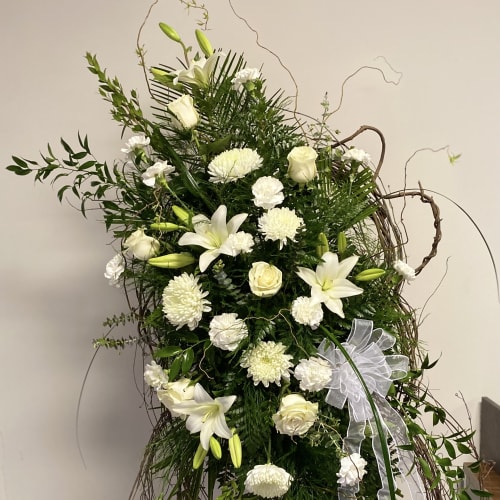 Tall white floral spray with lilies, roses, and ribbon on a twig frame