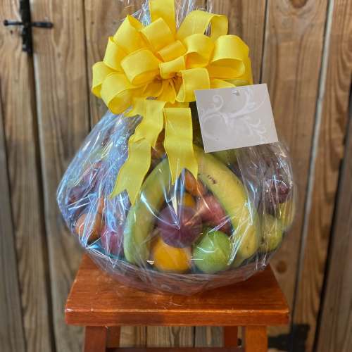 Wrapped fresh fruit basket with yellow bow and card on a wooden stool