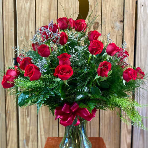 Tall arrangement of red roses with white filler flowers in a clear glass vase with a red bow.