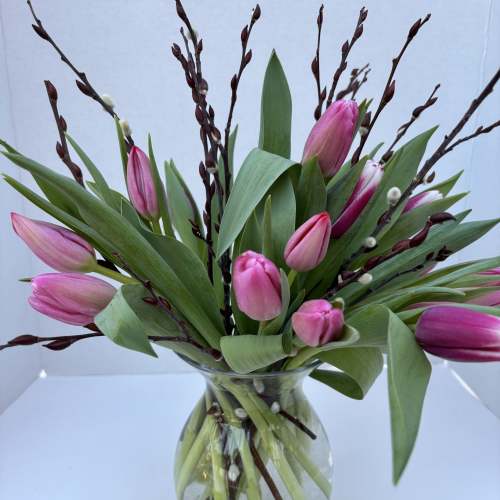 Pink tulips arranged in a clear glass vase with tall branches