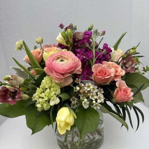 Mixed bouquet of pink, peach, yellow, and purple flowers in a glass vase