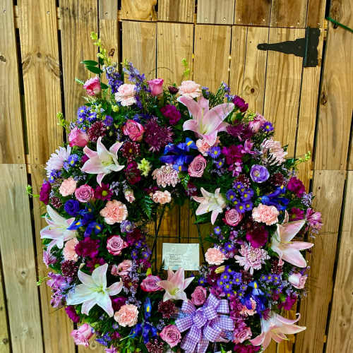 Heart-shaped floral wreath with pink, purple, and white blooms on a stand