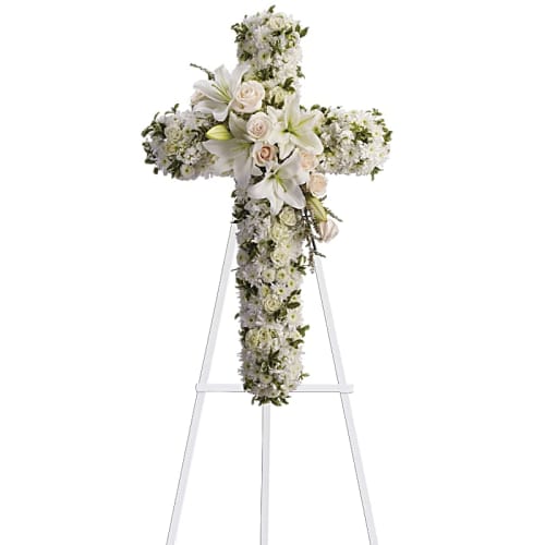 White floral cross on a stand with lilies and roses