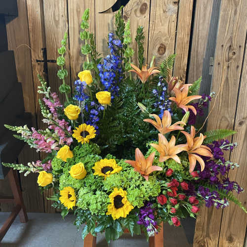 Tall floral arrangement with sunflowers, roses, lilies, and blue delphinium