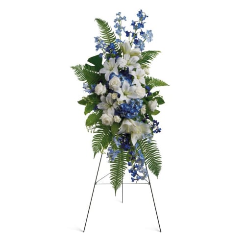 Standing floral spray with white lilies and blue flowers on a metal easel