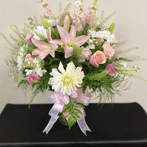 Pink lilies and white daisies in a glass vase with a pink ribbon