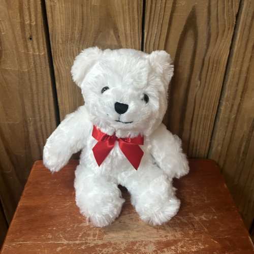 Small white teddy bear with a red bow sitting on a wooden surface.