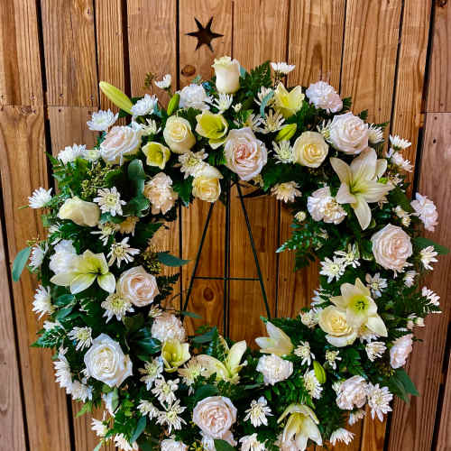 White floral wreath on a metal stand with roses and lilies