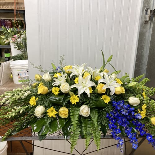 Low floral arrangement with white lilies, yellow roses, and blue flowers