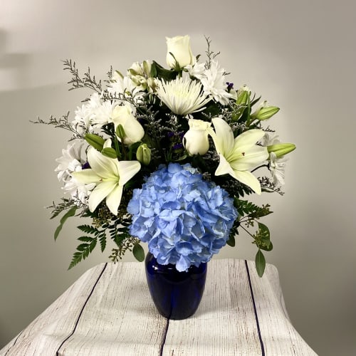 White lilies and daisies with a blue hydrangea in a dark vase