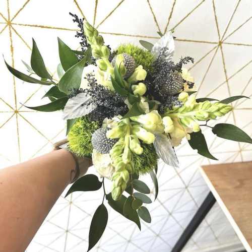 Handheld bouquet with pale yellow flowers, green accents, and silver foliage