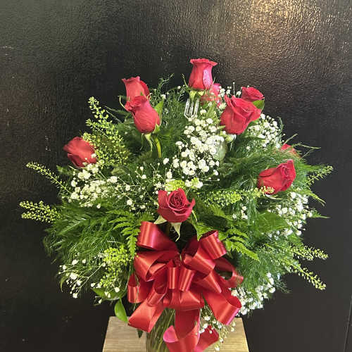 Red rose arrangement in a clear glass vase with a large red ribbon