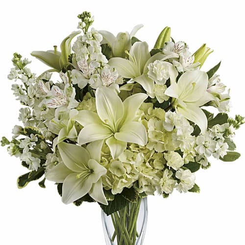 White lilies and mixed white flowers in a clear glass vase