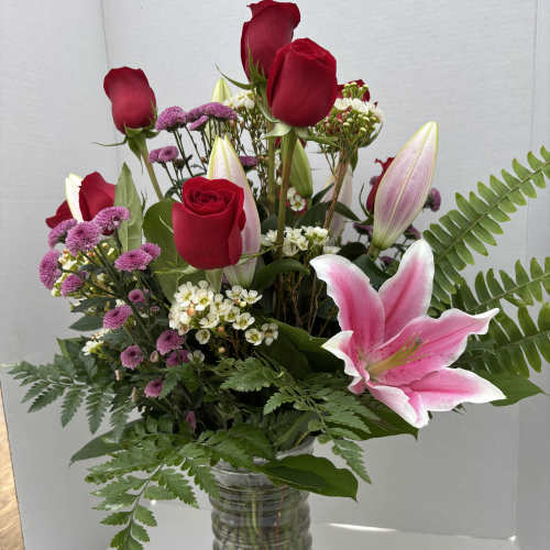 Mixed bouquet of red roses, pink lilies, and purple flowers in a glass vase