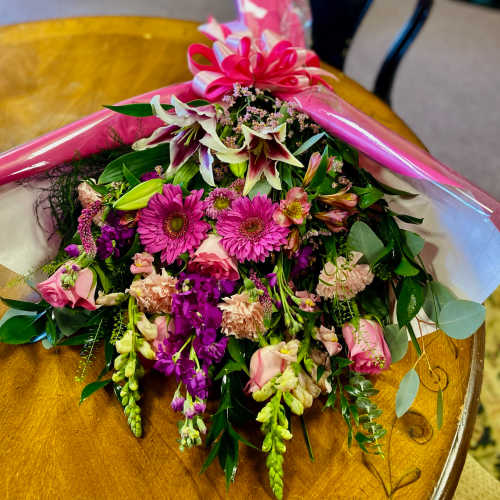 Bouquet of pink and purple flowers wrapped in pink paper with a bow