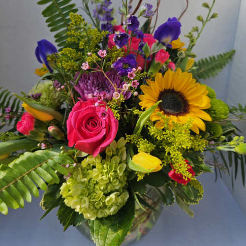 Mixed bouquet with a pink rose, sunflower, and purple blooms in a glass vase
