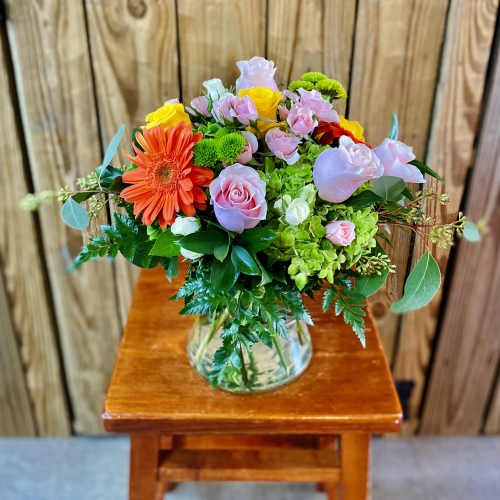 Mixed bouquet in a clear glass vase with pink roses and an orange gerbera daisy