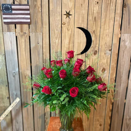 Red roses arranged in a glass vase with greenery