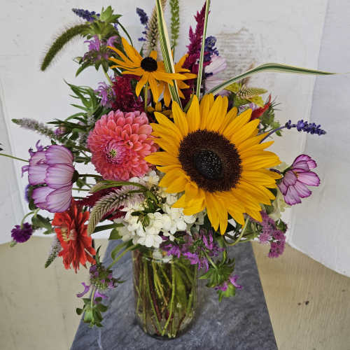 Mixed bouquet with sunflowers, pink blooms, and purple flowers in a glass vase