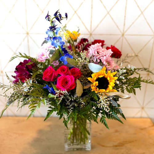 Mixed bouquet with roses, sunflowers, and blue flowers in a glass vase