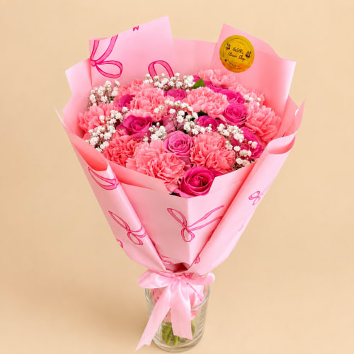 Pink bouquet of carnations and roses wrapped in pink paper in a glass vase