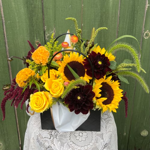 Mixed bouquet with sunflowers, yellow roses, and dark dahlias in a gift bag