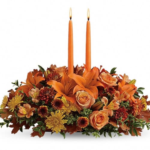 Orange floral centerpiece with two tall taper candles