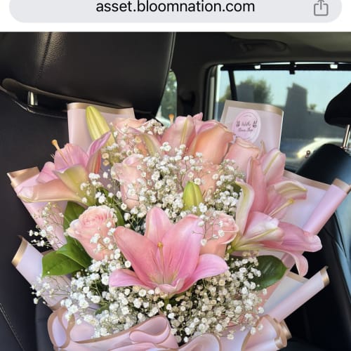 Large bouquet of pink lilies, roses, and white filler flowers wrapped in pink paper with ribbon