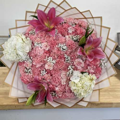 Pink carnation bouquet with lilies and white hydrangeas in layered wrap