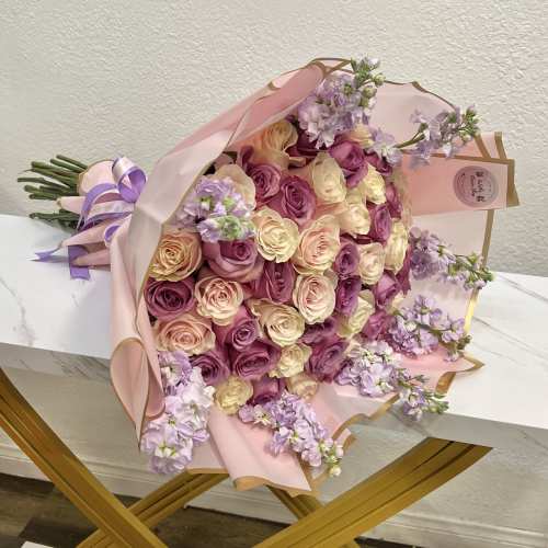 Bouquet of pink, cream, and lavender roses wrapped in pale pink paper