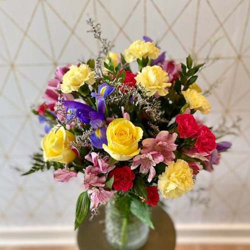 Mixed bouquet of roses, carnations, and purple flowers in a glass vase