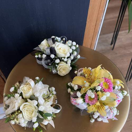 Three small floral bouquets with white roses and yellow blooms on a round table.