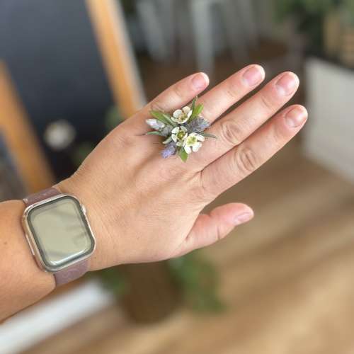 Hand wearing a small floral ring with white and lavender blossoms