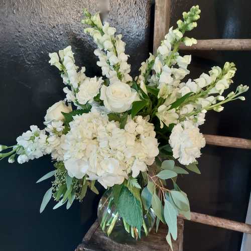 White floral arrangement in a clear glass vase with tall snapdragons and roses