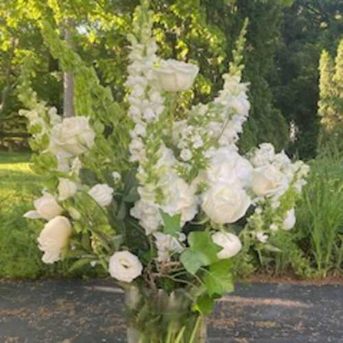 Tall white floral arrangement in a clear glass vase outdoors
