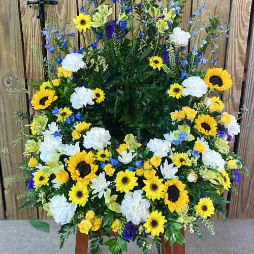 Large standing floral spray with sunflowers, white carnations, and blue flowers