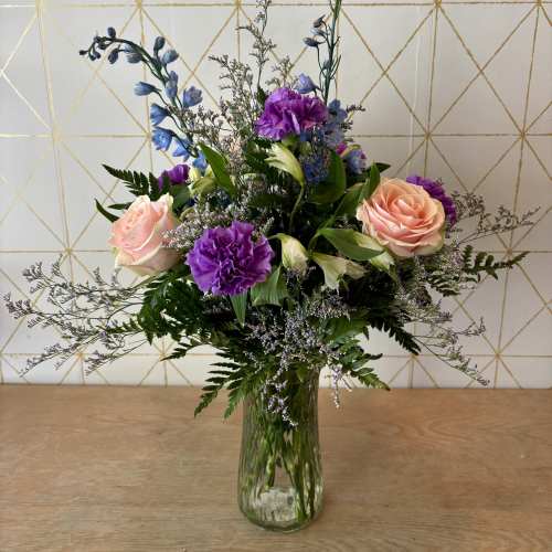 Mixed bouquet of pink roses and purple flowers in a glass vase