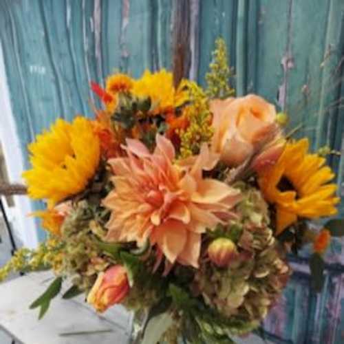 Bouquet of sunflowers, peach dahlias, and roses in a glass vase