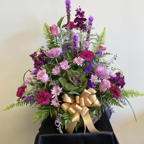 Pink and purple mixed flower arrangement with a gold ribbon in a basket